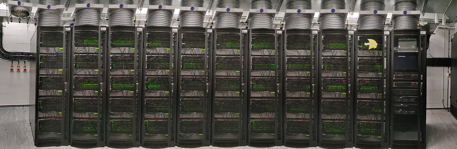 A panoramic shot of SpiNNaker 1 in 2018, which has over 1 million cores, housed in the Kilburn building in Manchester. The machine has a total of 1,036,800 cores and over 7 Terabytes of RAM, composed of 57,600 processing nodes, each with 18 ARM968 processors and 128 MB of mobile Double Data Rate Synchronous Dynamic Random-Access Memory (DDR SDRAM). For scale, each of the eleven server racks in this picture are around 600mm wide. (Furber et al. 2013) Version 2.0 of SpiNNaker has 10 million cores, completed in 2022. (Furber and Mayr 2022) CC BY-SA Panorama picture by Petruț Bogdan on Wikimedia Commons w.wiki/8Z3J